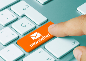 Ein Finger tippt auf eine orangene Taste auf einer Tastatur, auf der ein Briefsymbol zu sehen ist und das Wort "Newsletter".